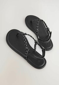 Black sandals with a flat sole, featuring a textured upper and braided straps with white accents for adjustable fit. Simple design.
