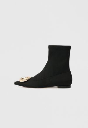 Schwarze Stiefeletten mit spitzem Zeh, aus glattem Stoff. Mit einem goldenen dekorativen Akzent an der Vorderseite und einem flachen Absatz.