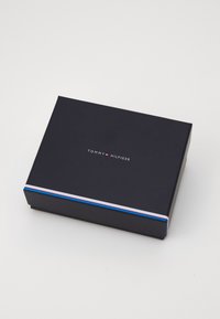 Svart rektangulær boks med matt finish, med et hvitt, rødt og blått stripemønster og "TOMMY HILFIGER"-logoen sentrert på toppen.