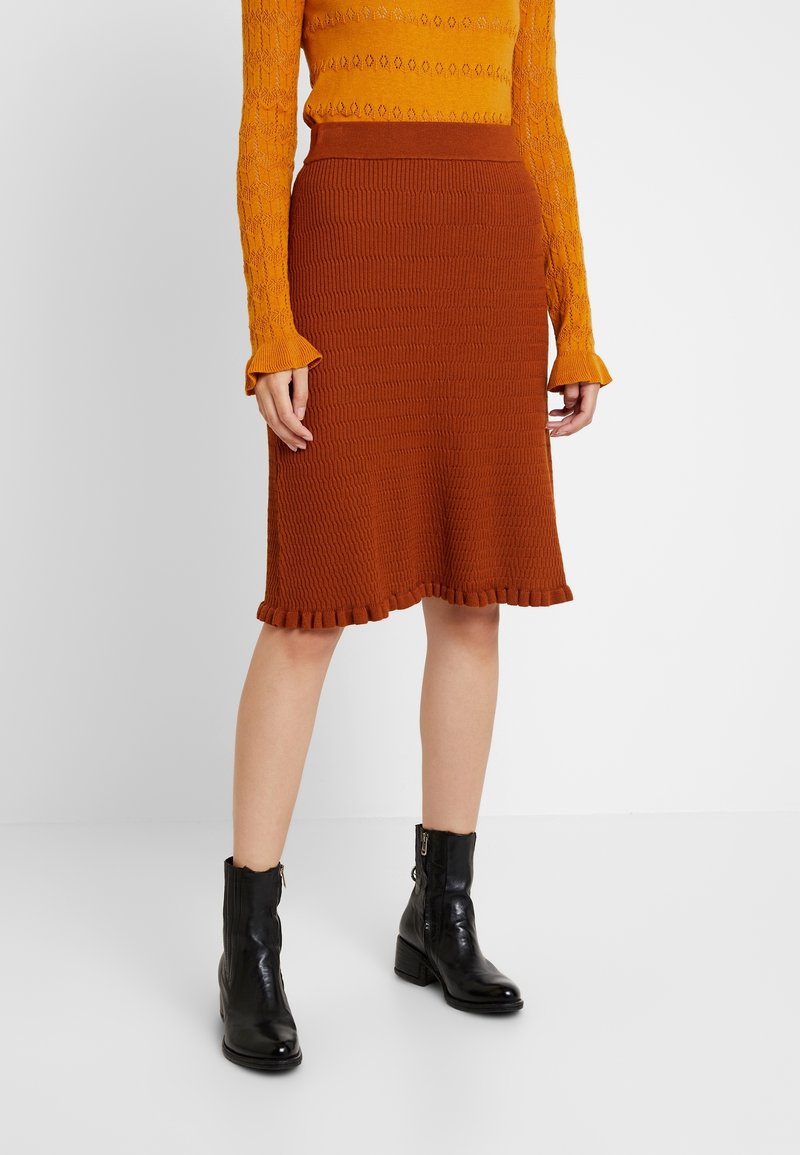 Stickad brun midiklänning med volangkant, ihop med en texturerad orange långärmad topp och svarta ankelskor.