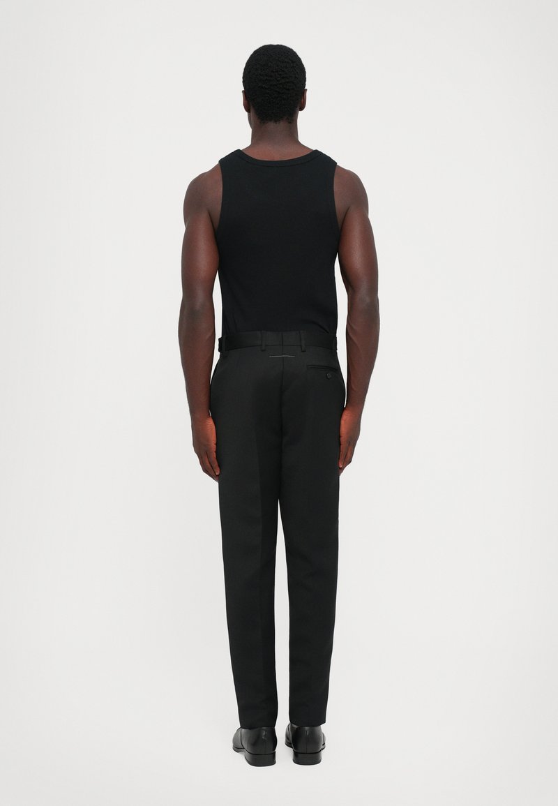 Zwarte tanktop gecombineerd met zwarte broek; slim fit met een gladde textuur. De broek heeft een achterzak en een riem.