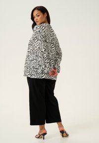 Blouse à motif de feuilles noir et blanc avec une coupe décontractée, associée à un pantalon large noir et des sandales à talons noires. Texturé en tissu lisse.