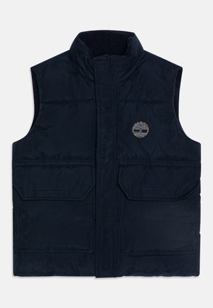 Gilet sans manches matelassé bleu marine avec col montant, deux poches à rabat à l'avant et petit logo d'arbre sur la poitrine gauche.
