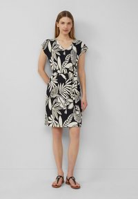 Blumenmuster-Kleid mit V-Ausschnitt, kurzen Ärmeln und tailliertem Bund in Schwarz und Cremefarben. Kombiniert mit hellbraunen Sandalen.