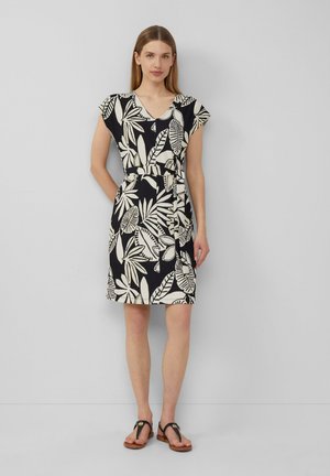 Blumenmuster-Kleid mit V-Ausschnitt, kurzen Ärmeln und tailliertem Bund in Schwarz und Cremefarben. Kombiniert mit hellbraunen Sandalen.