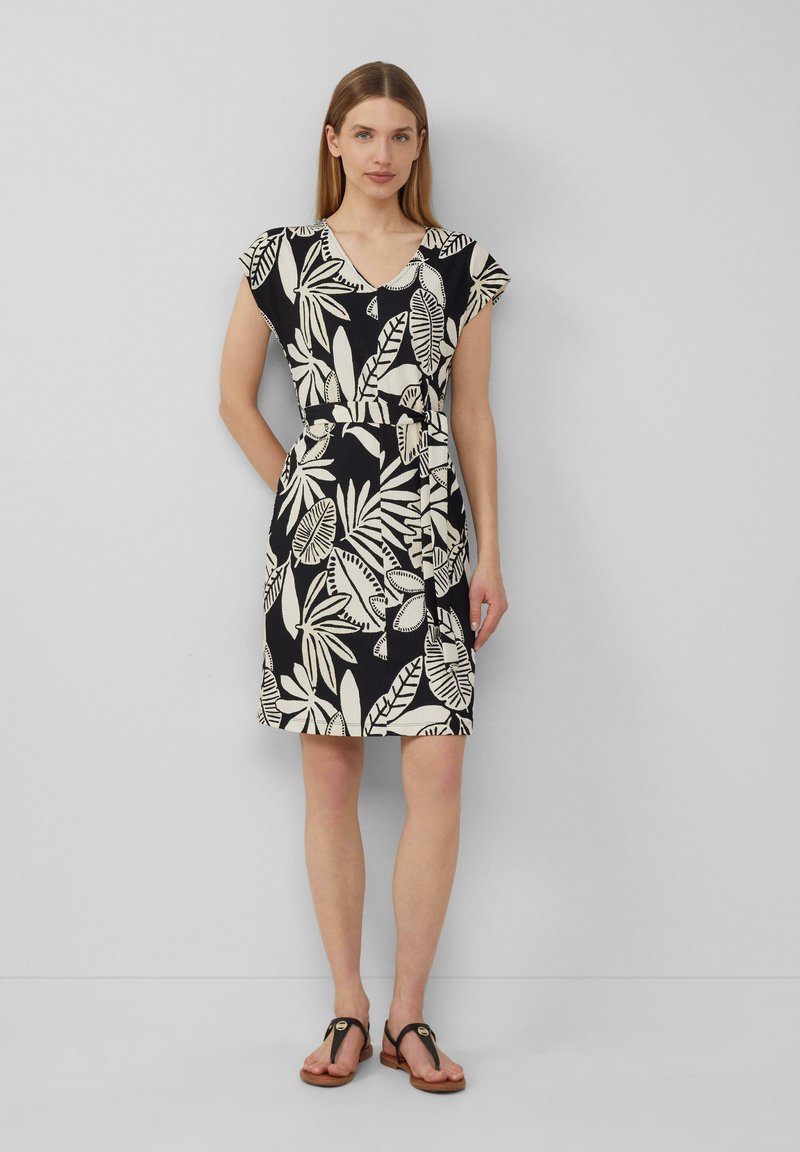 Blumenmuster-Kleid mit V-Ausschnitt, kurzen Ärmeln und tailliertem Bund in Schwarz und Cremefarben. Kombiniert mit hellbraunen Sandalen.