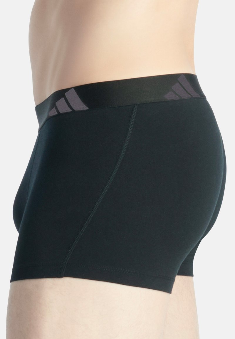 Zwarte katoenen trunk shorts met een gladde textuur, met een donkere tailleband met drie grijze strepen. Zijaanzicht dat de pasvorm en stofdetails benadrukt.