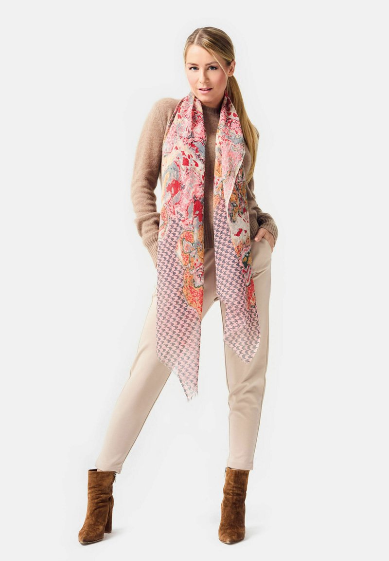 Floral pink and orange scarf with houndstooth accents, framed by a beige sweater and tan pants, paired with brown suede heeled boots.