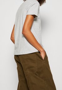 Grijs T-shirt met korte mouwen en een relaxte pasvorm, gecombineerd met olijfgroene werkbroek met textuurdetails en zijzakken.