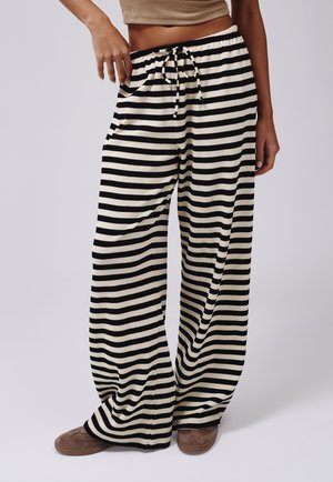 Pantalones de pierna ancha a rayas negras y crema con cintura ajustable con cordón y textura acanalada suave, combinados con calzado marrón.