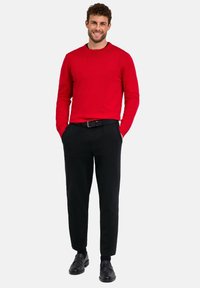 Pull en tricot rouge avec un col rond, associé à un pantalon noir sur mesure. Une ceinture et des chaussures noires complètent la tenue.