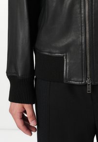 Black leather bomber jacket featuring ribbed cuffs and hem, silver zipper, and a side pocket detail. Smooth texture and fitted design.