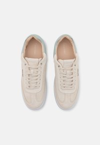 Sneakers in suede beige con un accento verde menta sul tallone, caratterizzati da suole bianche, lacci tondi e dettagli del logo sul lato.