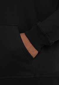 Black hoodie featuring a kangaroo pocket, ribbed cuffs, and hem. The fabric appears soft with a smooth texture and simple design.
