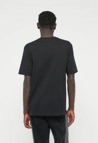 Μαύρο βαμβακερό μπλουζάκι με στρογγυλή λαιμόκοψη, κοντά μανίκια και άνετη εφαρμογή. Διαθέτει λείο υφή και απλό, μινιμαλιστικό σχέδιο.