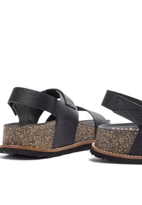 Sandali neri in pelle con cinturini incrociati, piattaforma in sughero e suola in gomma. Cinturino regolabile con chiusura a strappo.