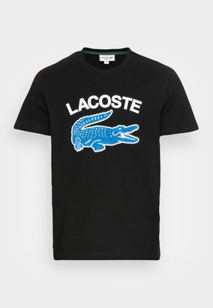 Sort T-shirt med korte ærmer med hvid "LACOSTE" tekst og stor blå krokodille grafik centreret på brystet.