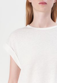 Hvid bomulds t-shirt med rund hals, korte opsvungneærmer og en blød, tekstureret finish. Simpelt design med minimal detaljer.