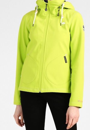 Person trägt eine leuchtend limettengrüne Jacke mit Reißverschluss und Kapuze sowie weißen Kordeln, kombiniert mit schwarzen Hosen.