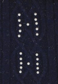 Marineblaues Strickgewebe mit einem strukturierten Muster, geschmückt mit weißen perlenähnlichen Perlen, die in zwei vertikalen Linien angeordnet sind.