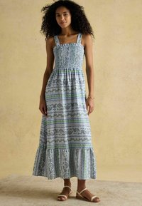 Dlhé šaty bez rukávov so smockovaným živôtikom v modro-bielom kvetinovom vzore. Majú rozšírený lem a tenké ramienka. Ľahká, vzdušná textília.