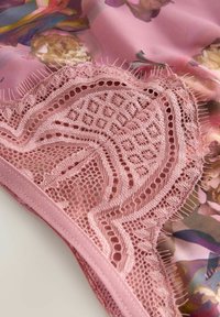 Rózsaszín csipke részletek virágmintás háttérrel; bonyolult mintákkal és rojtokkal a szélén, kiemelve a textúrát és a dizájnt.