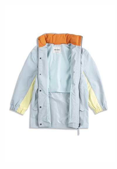 Veste bleu clair avec manches jaunes, doublure de col orange, fermeture éclair frontale, boutons-pression et étiquette intérieure visible.