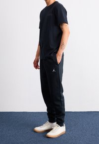 Svart t-shirt med kort ärm och liten logotyp, parat med svarta sweatpants med en vit Air Jordan-logotyp, och vita sneakers med gummisålar.