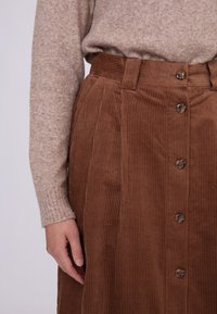Brun kordfløjlskørt med lodrette ribber, der har en høj talje og fem knapper foran. Sweater i lys beige.