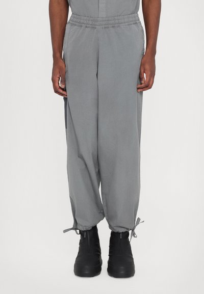 Pantalons gris amples avec taille élastique, poignets resserrés et poches latérales, associés à des bottes noires à la cheville. Texture douce.