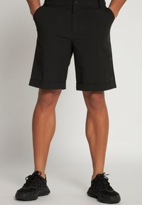 Shorts noirs en matériau léger, avec un ourlet replié et une poche zippée sur le côté. Associés à des chaussures de sport noires.