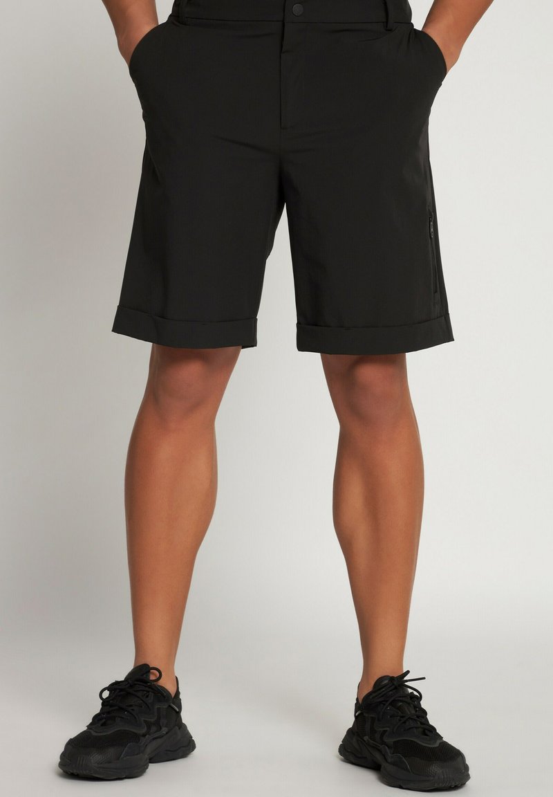 Pantalones cortos negros hechos de un material ligero, con un dobladillo plegado y un bolsillo con cremallera en el lateral. Combinados con zapatillas deportivas negras.