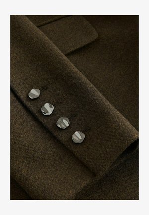 Tessuto di lana marrone con una texture morbida, caratterizzato da quattro bottoni argentati lucidi e curvi sul polsino per un dettaglio aggiuntivo e la chiusura.