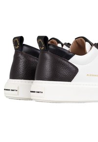 Sneakers bianchi in pelle con dettagli in pelle marrone testurizzata, dotati di una suola bianca spessa e etichette del marchio in nero e oro.