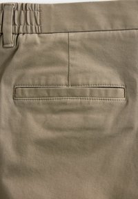 Beige püksid, millel on tagatasku puhta viimistlusega, kanga tekstuur näitab peent soonikut ning mugav elastne vöökoht.
