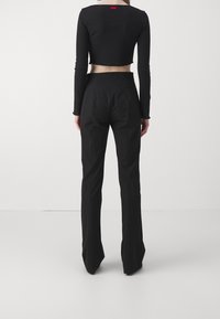 Haut noir cropped à manches longues avec une couture brute et étiquette de logo ; pantalon noir taille haute avec une coupe ajustée et jambes évasées.