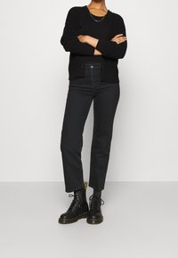 Černý pletený cardigan s knoflíky, černé džíny s vysokým pasem a černé šněrovací boty se žlutými akcenty. Jednoduchý, strukturovaný design.