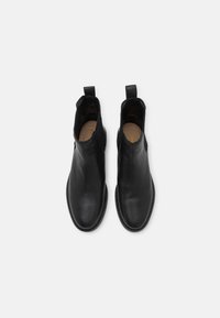 Botas de tobillo negras de cuero con una textura lisa, puntera redondeada, paneles laterales elásticos y lengüetas para un fácil calzado. Suela de goma plana.