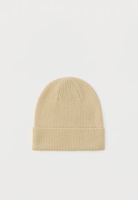 Bež kapa od rebrastog vunenog pletiva s presavijenim rubom, položena ravno na jednostavnoj bijeloj pozadini.