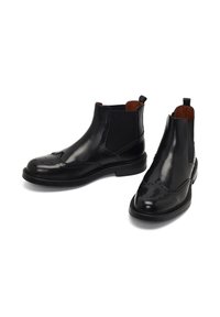 Botas de cuero negro hasta el tobillo con paneles elásticos en los laterales, detalles de brogue en la punta y una lengüeta para facilitar su uso. Observa el acabado texturizado.