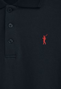 Svart polo tröja med texturerad tyg, prydd med tre svarta knappar och en röd broderad golfare-logga på vänster bröst.