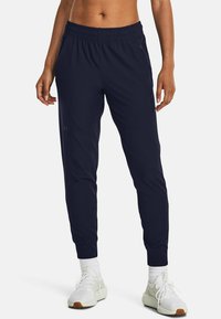 Navy tapered athletic pants with an elastic waistband, side pockets, and textured fabric. Paired with white sneakers and ankle socks.