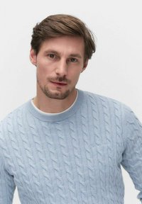 Lichtblauwe kabelgebreide trui met een ronde hals en een klein zakje op de linkerborst. Zachte textuur en een casual pasvorm.