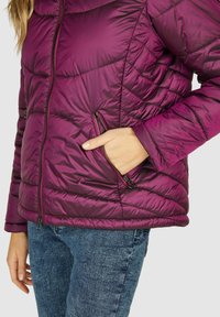 Paarse pufferjack met een doorgestikt patroon, ritszakken aan de zijkant en een gladde textuur, gecombineerd met blauwe jeans.