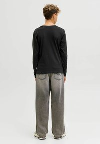 Zwart langhemd met lange mouwen, gecombineerd met oversized grijze denim broek. Opmerkelijke details zijn de stiksels en het ontwerp van de achterzak. Casual schoeisel maakt de look af.