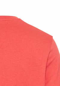 Koralrød t-shirt, korte ærmer, rund halsudskæring, blødt bomuldsstof, glat tekstur, enkelt design uden mønstre eller detaljer.