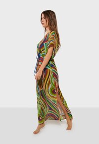 Kaftan long et coloré avec des motifs tourbillonnants en vert, rouge, bleu et jaune. Confectionné en tissu léger et transparent avec une fente latérale.