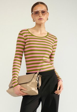 Donna con top a righe rosa e oliva a manica lunga, pantaloni neri, grande clutch beige, orecchini a cerchio dorati e occhiali da sole oversize.
