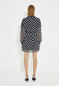 Zwart-witte gemusterde mini-jurk met lange, doorschijnende mouwen en een strakke taille. Bevat een geometrisch diamantpatroon en een uitlopende rok.