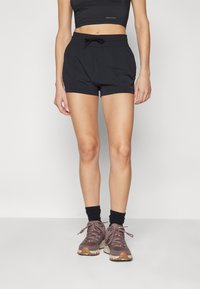 Pantalones cortos deportivos negros con cintura elástica y cordón. Estilizados con un top corto negro ajustado y botas de senderismo marrones.